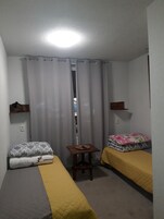 Una habitación pequeña y funcional con dos camas individuales, una mesita y un estante.