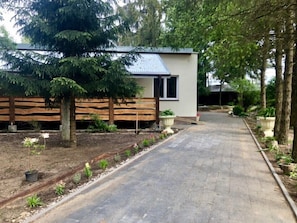 A modern house with a paved driveway, wooden fence, and a garden with various plants.