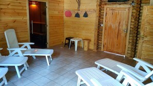 Interior de una cabaña de madera con sillones blancos, una mesita y un televisor montado en la pared.