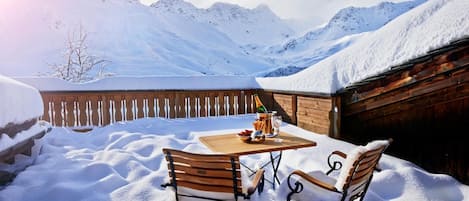 An outdoor wooden table with chairs set in a snowy landscape, with mountains in the background.