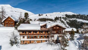 Un grand chalet en bois doté de nombreux balcons, entouré de montagnes et d’arbres couverts de neige.