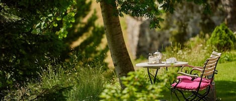 A table and chair set in a lush green outdoor area with a view of a stone wall.