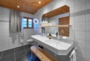 Ein modernes Badezimmer mit Holzboden, zwei Waschbecken, einer Toilette und einer Sitzbank.