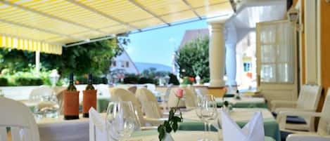 Un área de comedor al aire libre con mesas dispuestas para dos personas, con cristalería transparente y un centro de mesa con rosas.