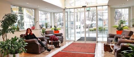 A spacious lobby with leather sofas, a red carpet, and potted plants.
