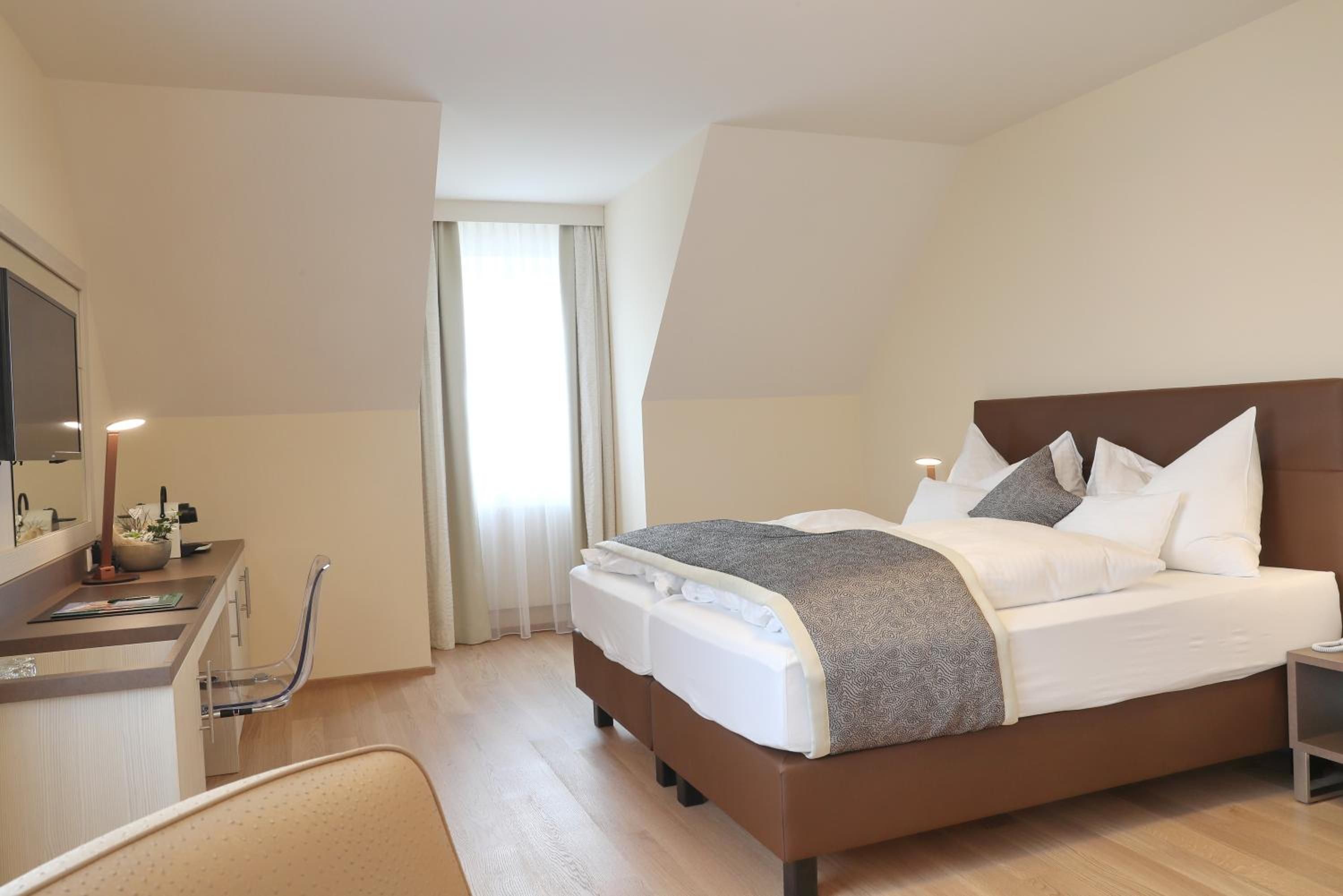 Ein Hotelzimmer mit Bett, Schreibtisch, Stuhl und einem fensterbepflanzten Fenster.