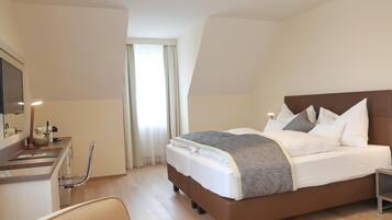 Ein Hotelzimmer mit Bett, Schreibtisch, Stuhl und einem fensterbepflanzten Fenster.