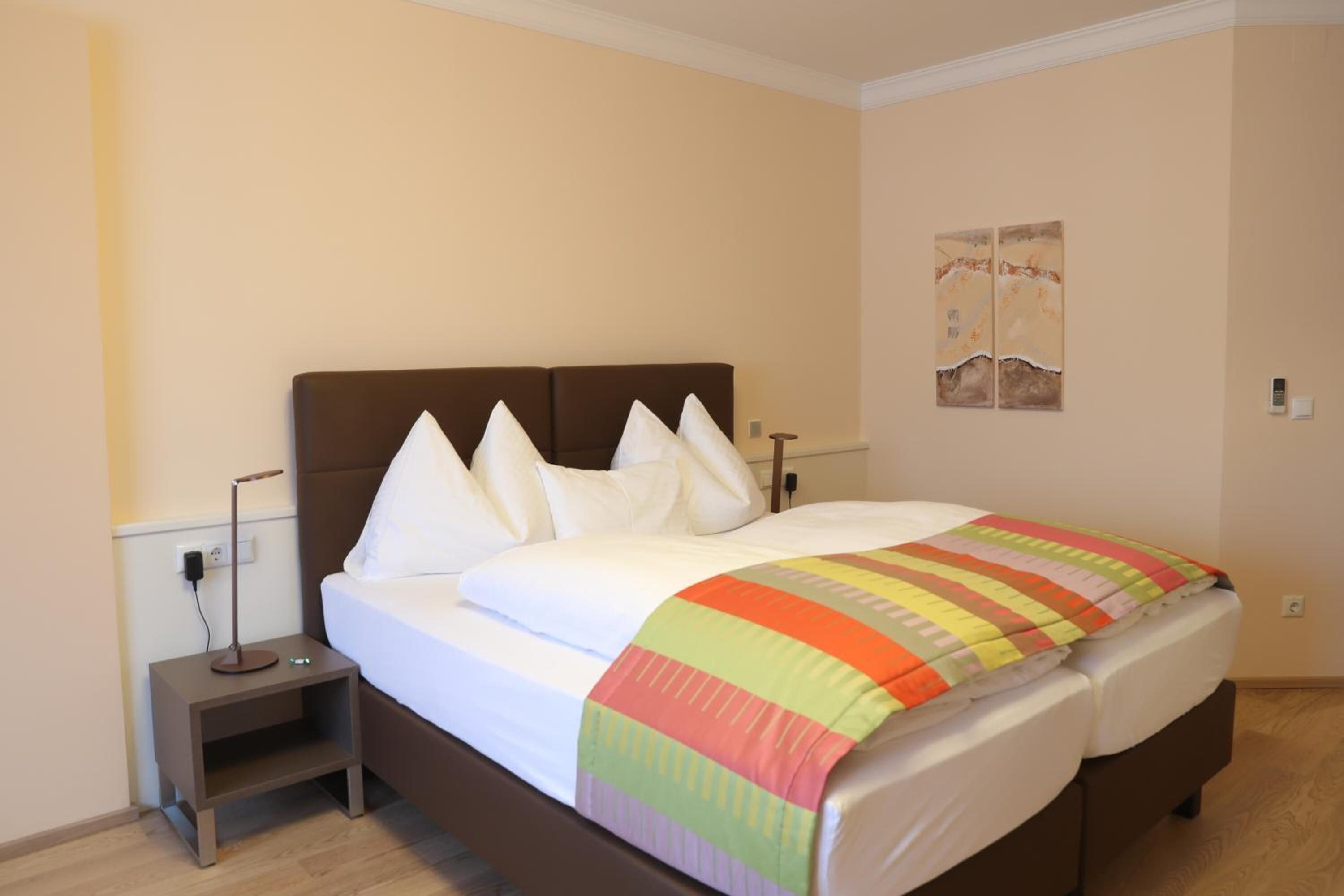 A hotel room with a bed, bedside table, lamp, and a wall-mounted artwork.