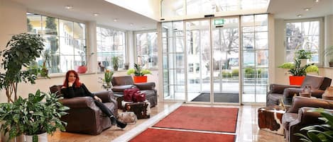 A spacious lobby with leather sofas, a red carpet, and potted plants.