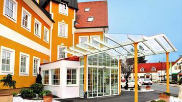 Ein Hotel mit Eingangsbereich, einem Wintergarten aus Glas, einem Gebäude mit rotem Dach und verschneitem Gelände.