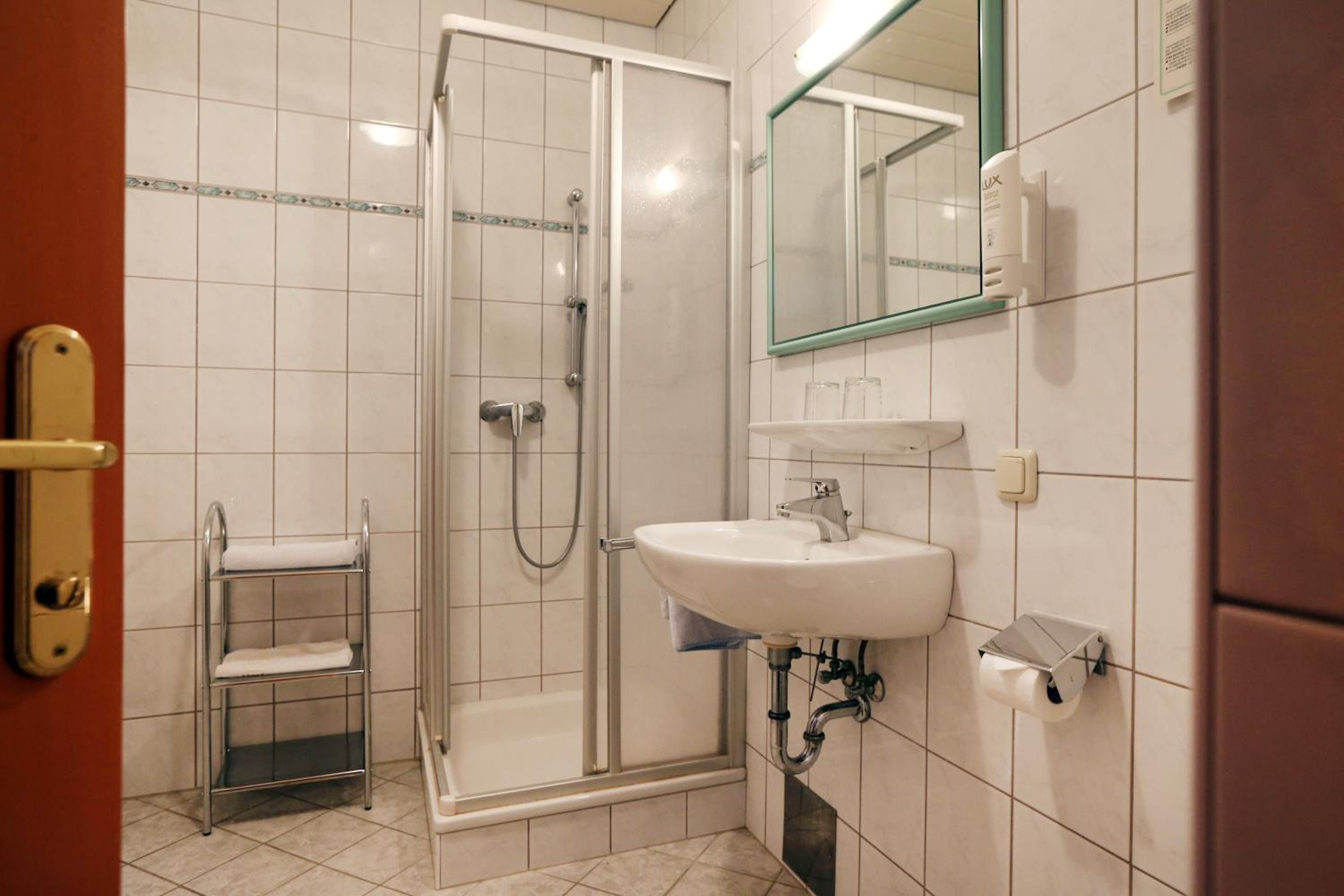 Un baño con cabina de ducha de vidrio, un lavabo blanco y un espejo encima.