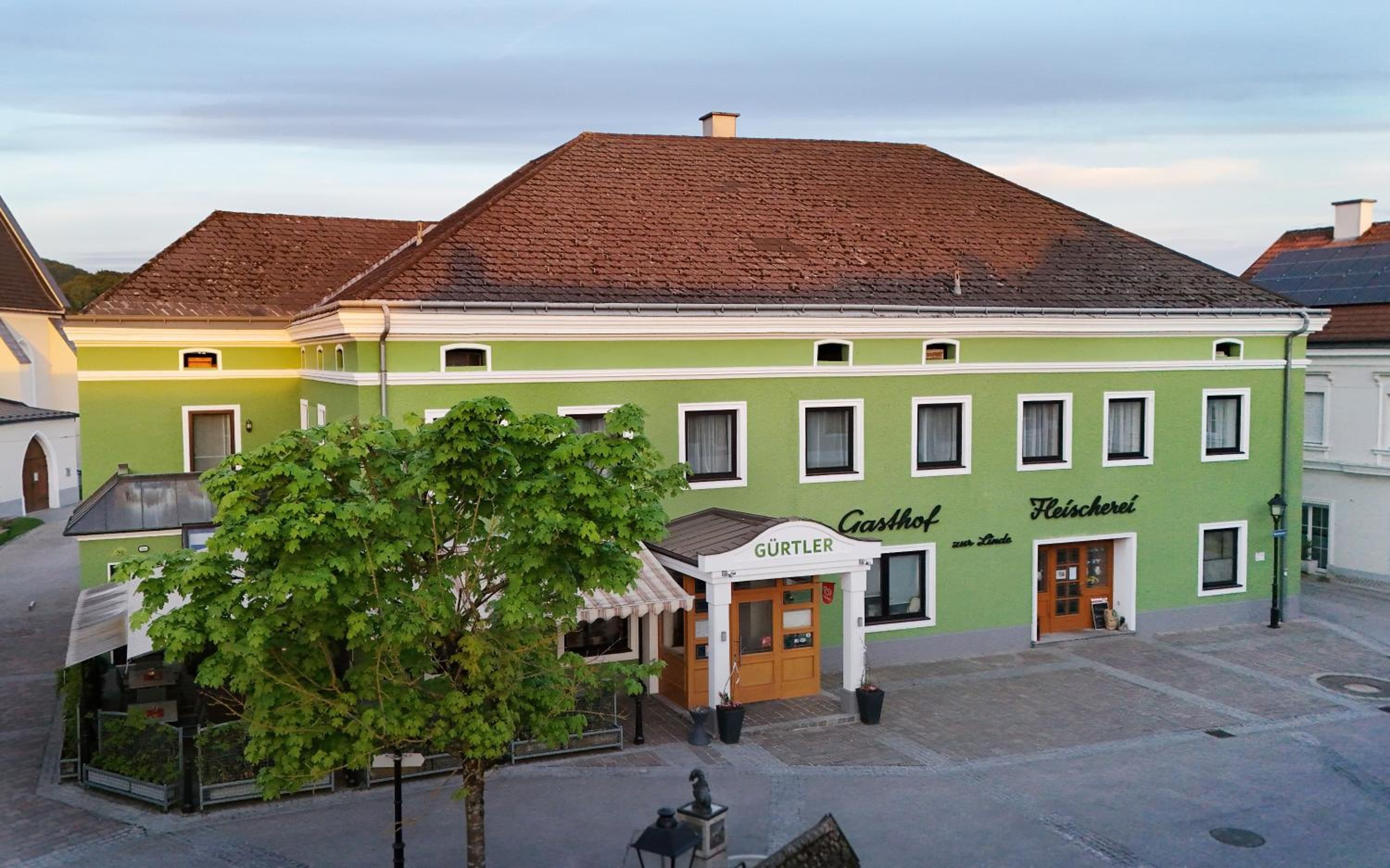 A two-story building with a green facade, a visible ground floor entrance, and a sign that reads 'Gürtlr Fleischerei.'