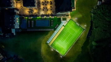 Vista aérea de un complejo deportivo con cancha de tenis, piscina y zona de asientos.