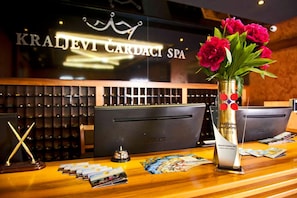 Una recepción con un cartel que dice 'KRAJLEVI CARDACI SPA', un florero con flores rojas, una campana y una exhibición de folletos.