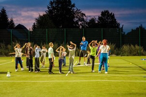 Un grupo de personas en un campo deportivo, con una valla verde y árboles al fondo.