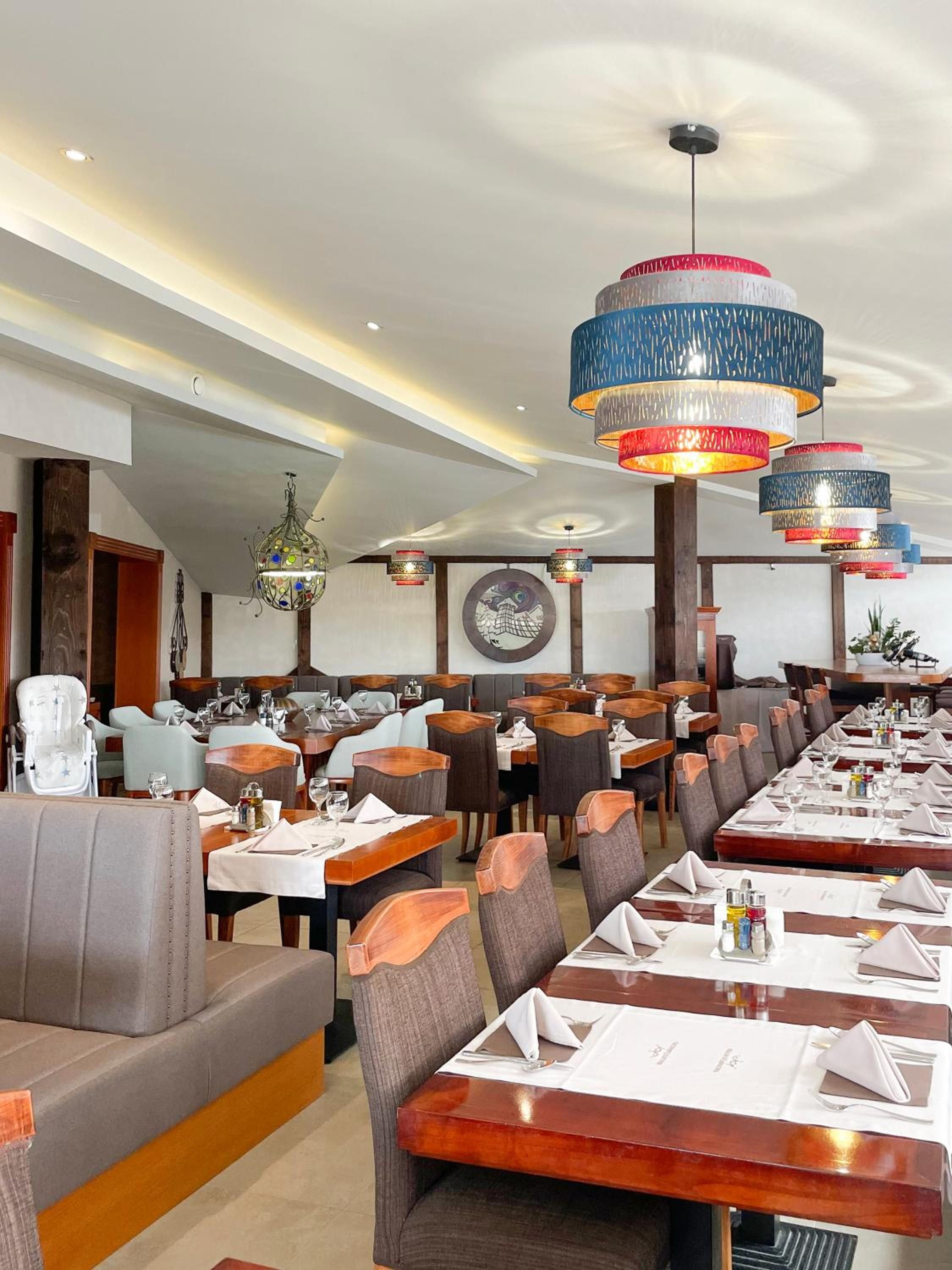 Ein Restaurant mit mehreren Tischen, Stühlen, einer Kristallleuchtre und einem Wandbild.