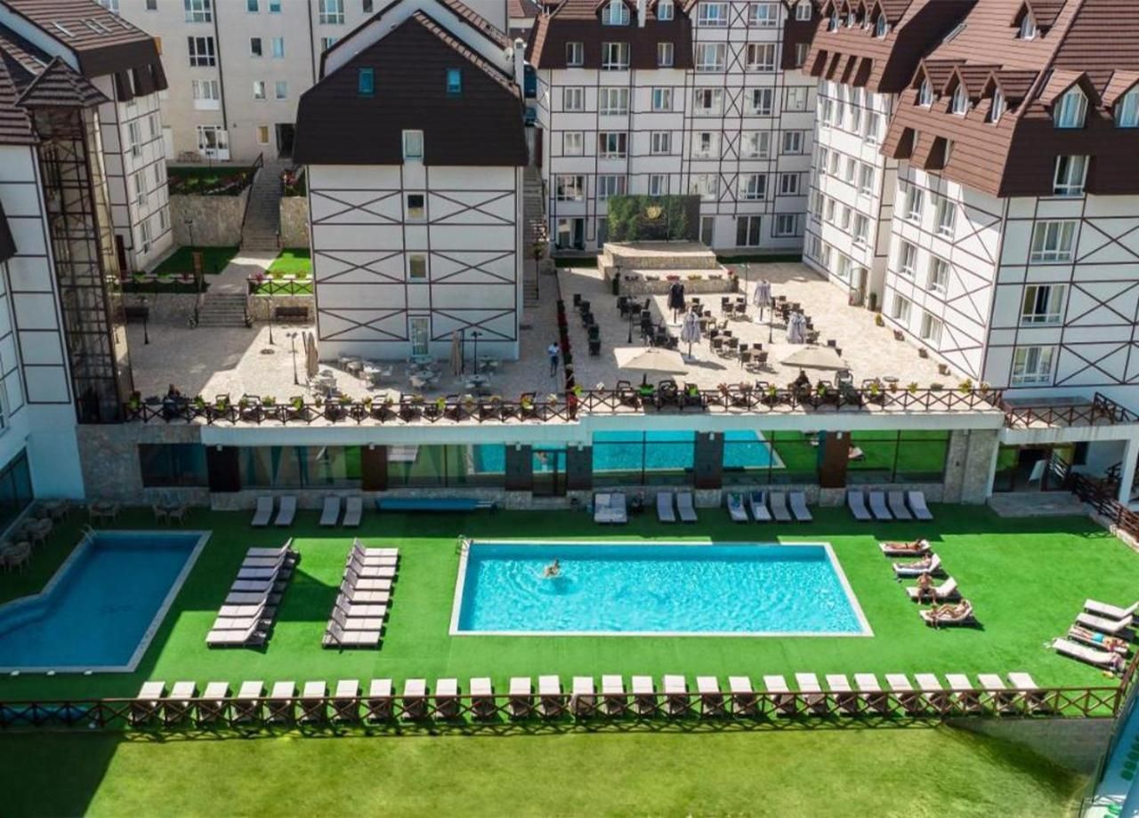 A hotel courtyard with two swimming pools, sun loungers, and a small garden area.