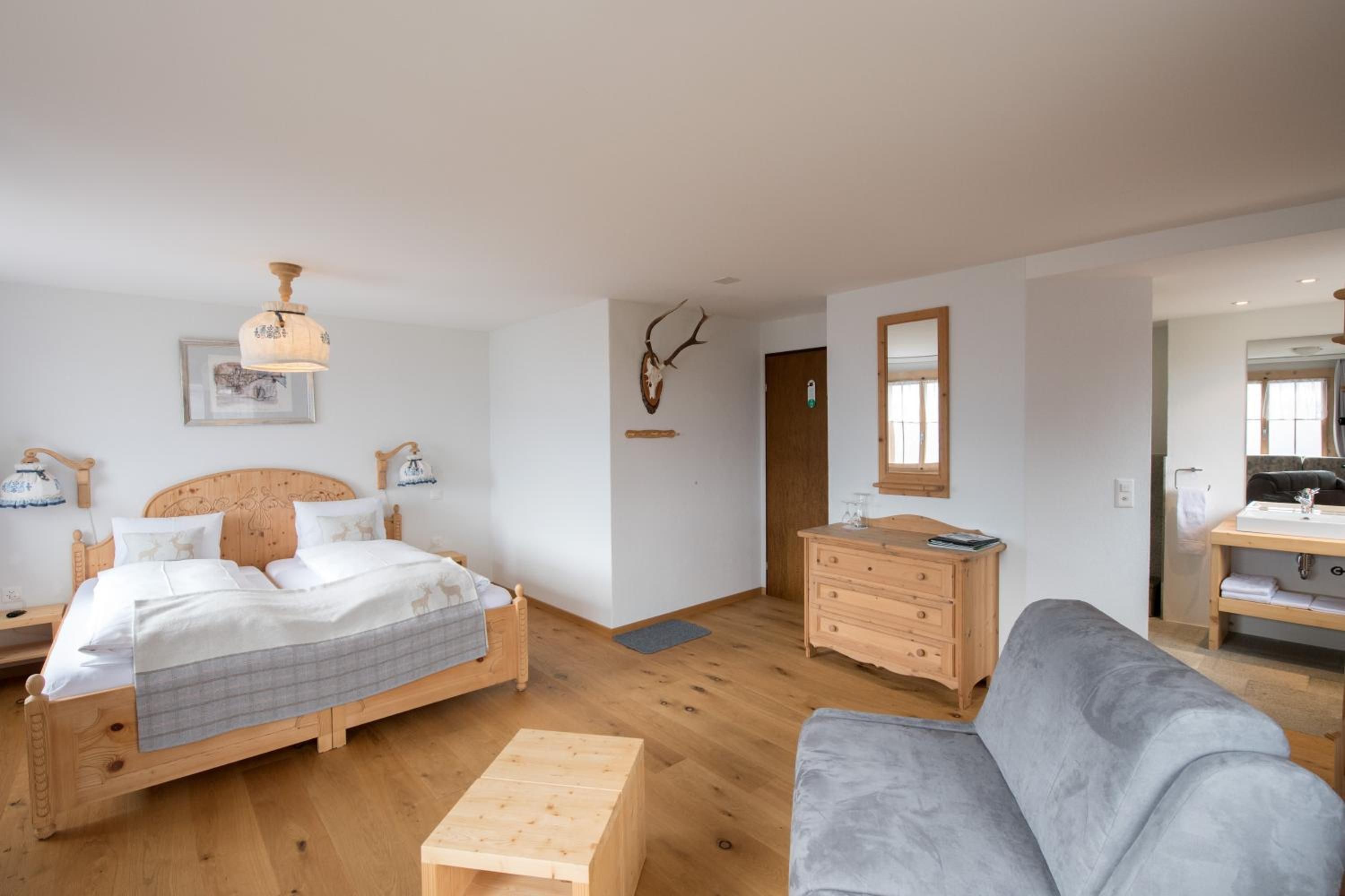 Een slaapkamer met een houten bed, een nachtkastje, een dressoir, een grijze bank en een houten salontafel.