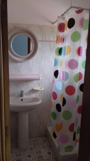 Ein Badezimmer mit einem weißen Waschbecken, einem Spiegel und einem Duschvorhang mit bunten Punkten.