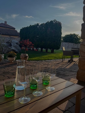 A patio with a table set for a meal, surrounded by a garden with trees and a stone wall.