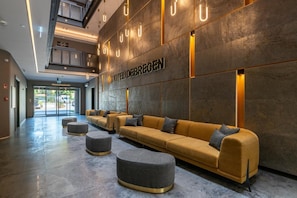 A hotel lobby with a reception desk, a long sofa with ottomans, and a modern design.
