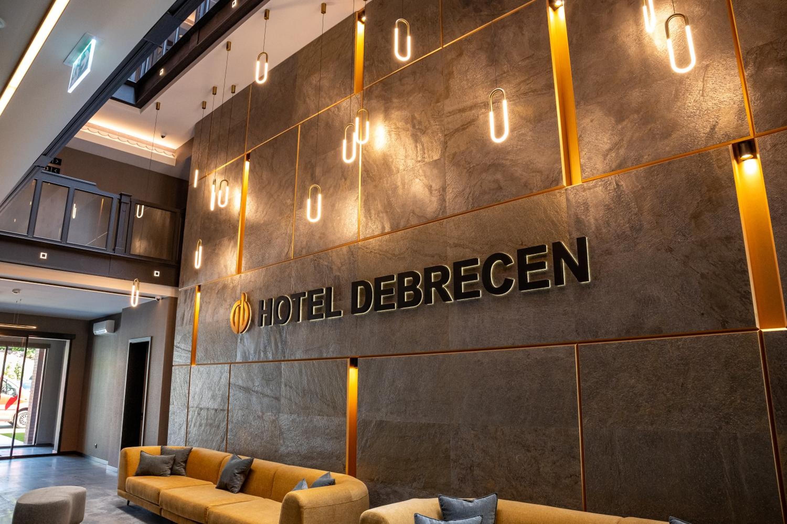A modern hotel lobby with a large sign reading 'HOTEL DEBRECEN' and a seating area with sofas.