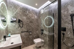 Un baño moderno con pared de mármol, un lavamanos, un inodoro y una zona de ducha con cabina de vidrio, con cabezal de ducha y secador de mano.