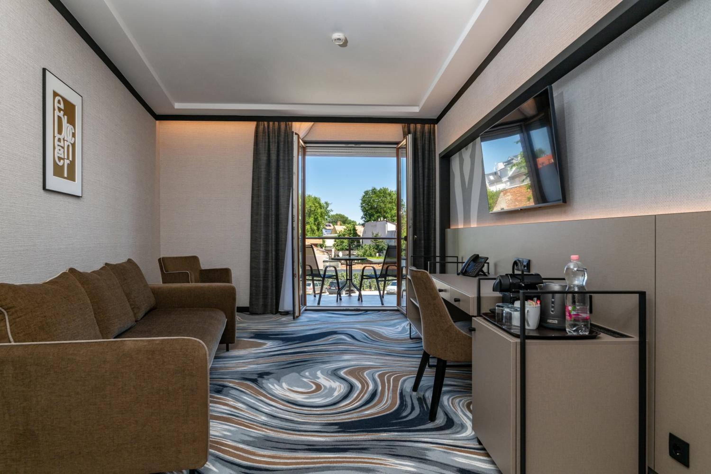 A hotel room with a sofa, a desk with a TV, and a view of the outdoors.