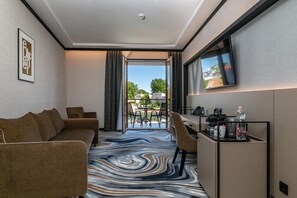Habitación de hotel con sofá, escritorio y televisor, y vista al exterior.