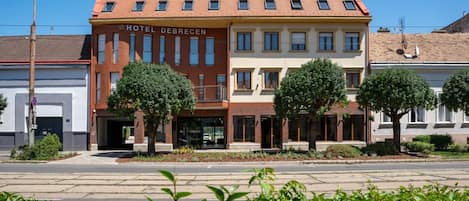 A hotel named 'HOTEL DEBRECEN' with a red and beige facade, multiple windows, and a parking garage entrance.