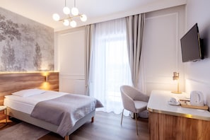 Habitación de hotel con cama, escritorio, silla, televisor y un amplio ventanal con cortinas.