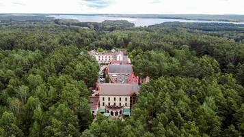 Un edificio grande de varios pisos rodeado de un bosque frondoso, con un lago al fondo.