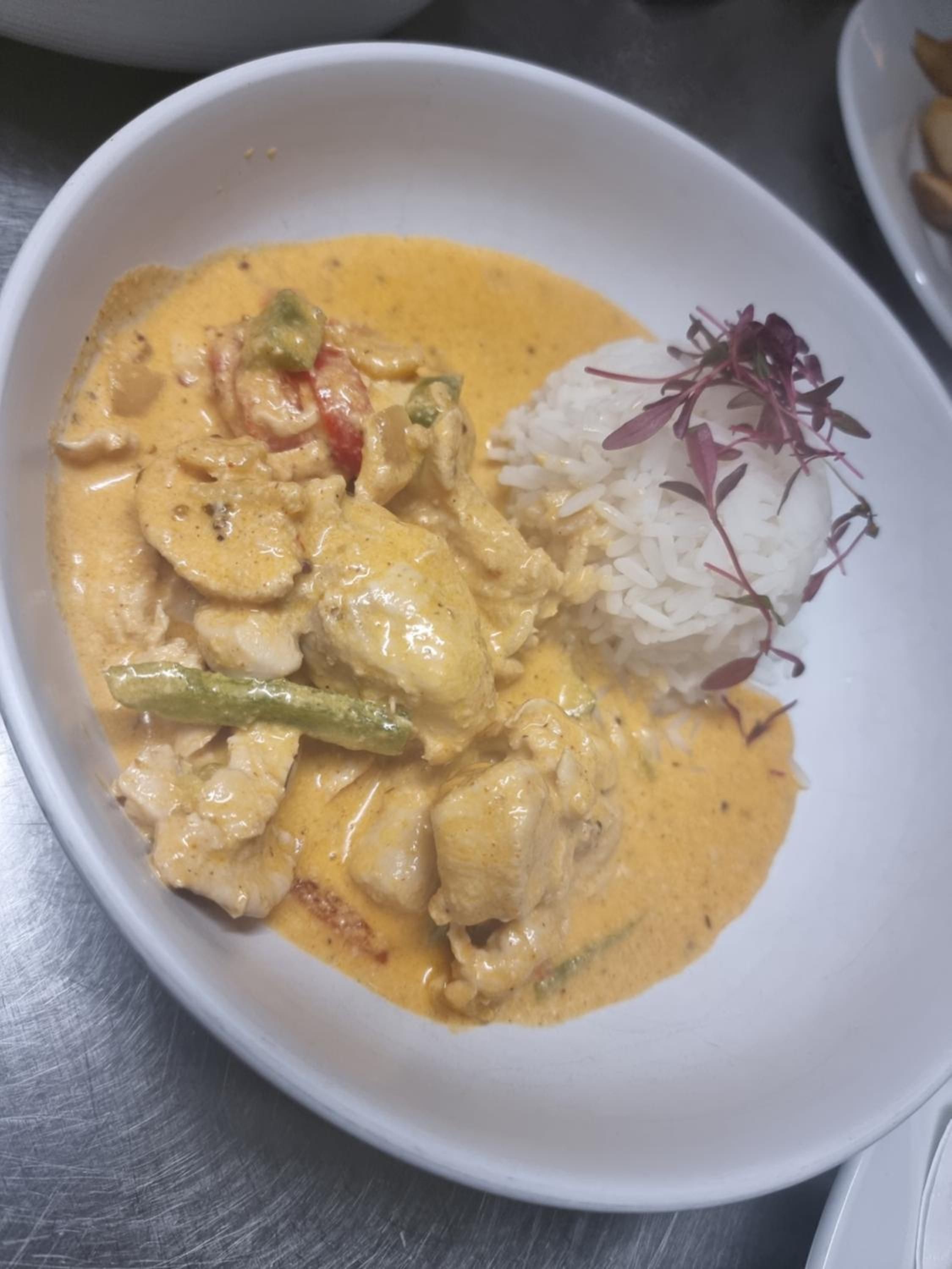 A bowl of creamy chicken curry with vegetables and white rice, garnished with herbs.