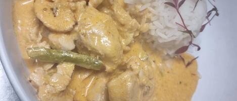 A bowl of creamy chicken curry with vegetables and white rice, garnished with herbs.
