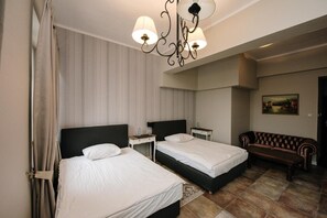 A hotel room with two beds, a bench, a small table, and a painting on the wall.