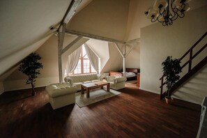 Quarto no sótão com teto inclinado, escada de madeira, um sofá, uma cama e um candelabro.