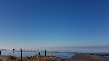 A coastal view with a clear sky, a sandy beach, and a fence.