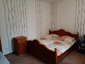 A bedroom with a wooden bed, a nightstand, and a patterned wall. - Goode Wind (Norden)