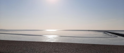 A beach with a clear sky and calm water reflecting the sun.
