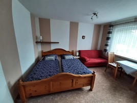 A bedroom with a wooden bed, a red sofa, a small table, and a window with curtains.