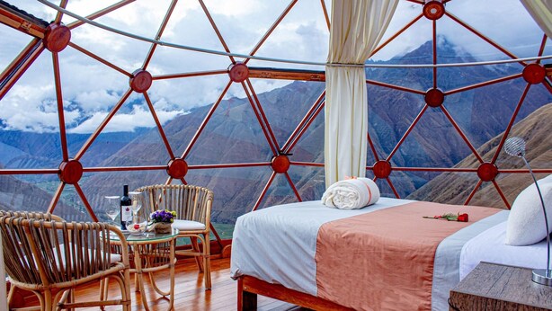 A room with a bed, a chair, a table, and a view of mountains. - Vertical Sky Luxury Suites (Ollantaytambo)