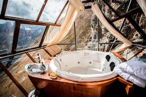 Una habitación con una bañera grande, un tocador de madera y vistas a un paisaje montañoso a través de amplios ventanales.