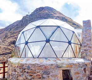 Una estructura de cúpula geodésica sobre base de piedra, con montañas al fondo.
