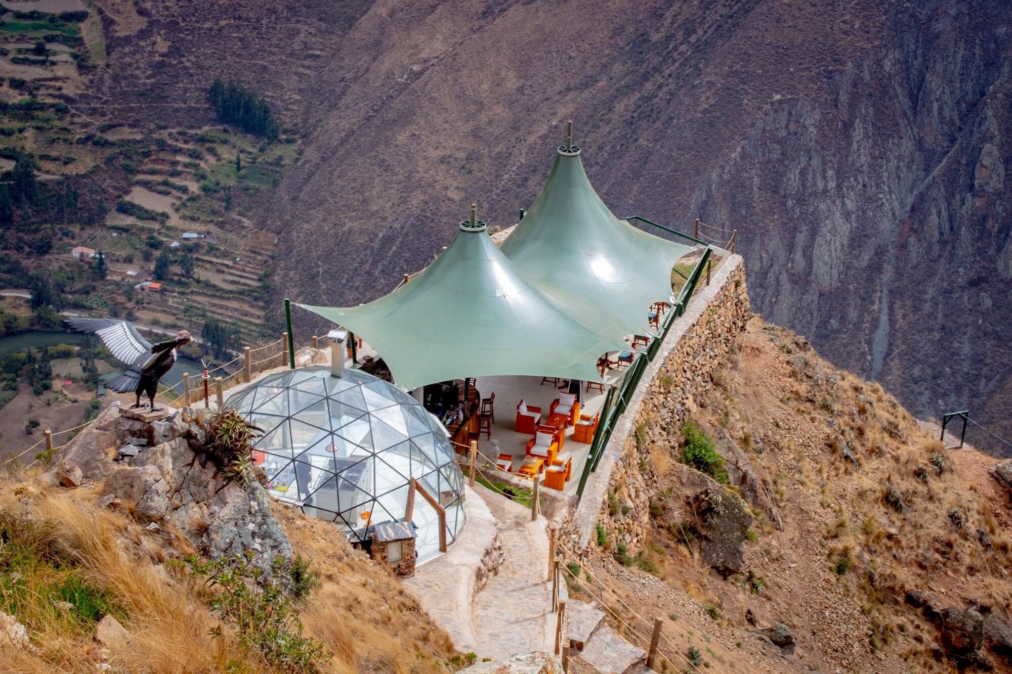 A mountain-side restaurant with a glass dome and green-roofed structures.