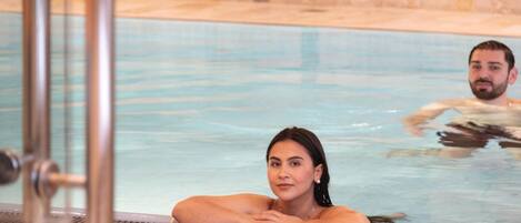 A pool area with tiled flooring and a glass partition.