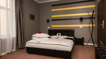A hotel room with a bed, a bedside table, a wall-mounted TV, and a window with curtains.