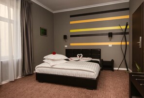 A hotel room with a bed, a bedside table, a wall-mounted TV, and a window with curtains.