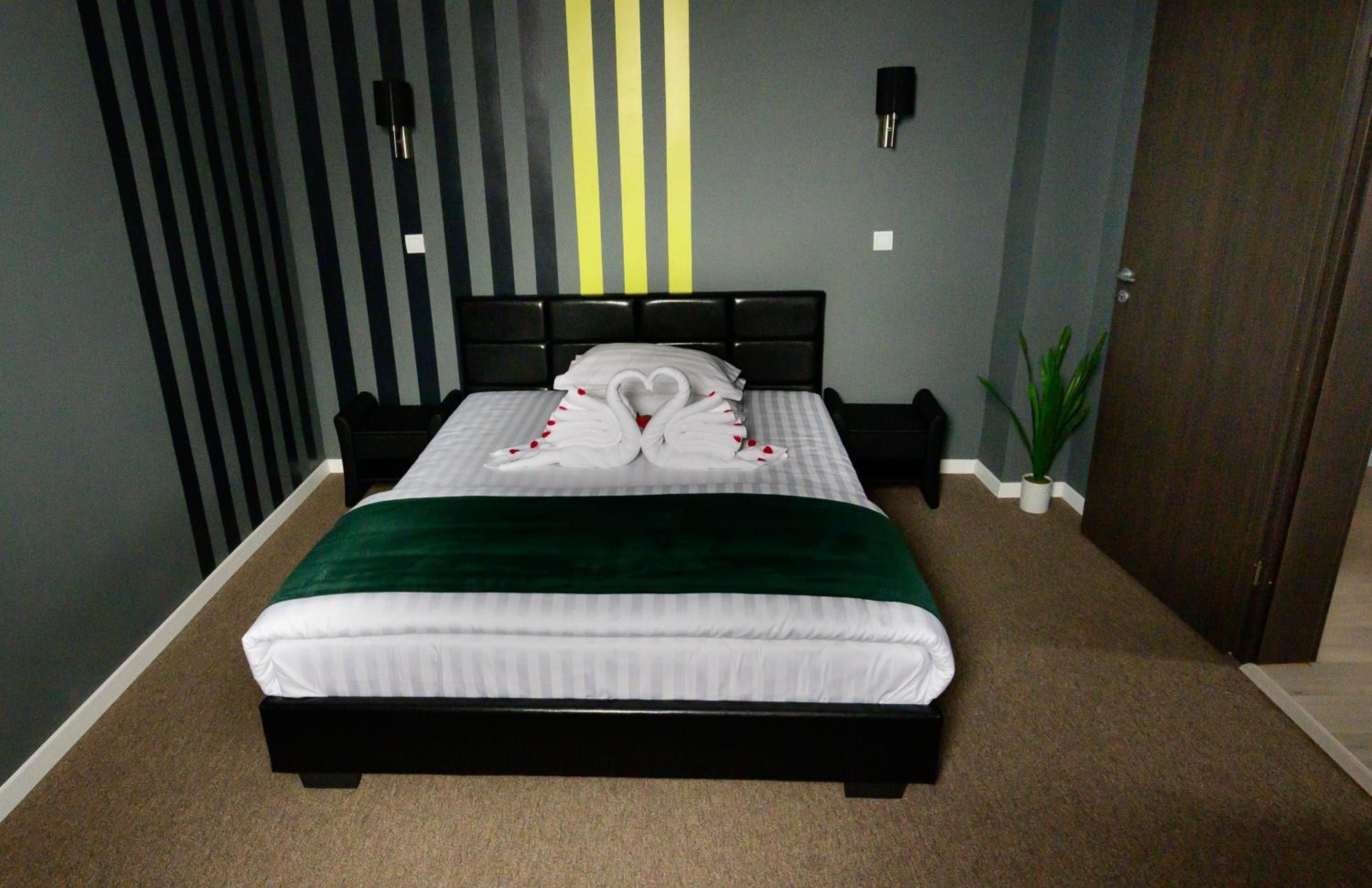 A bed with a heart-shaped towel arrangement, a green throw, and a dark headboard.