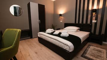 A hotel room with a bed, a green chair, a wardrobe, and a mirror.