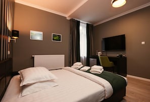 A hotel room with a bed, a desk, a chair, a flat-screen TV, and a window with curtains.